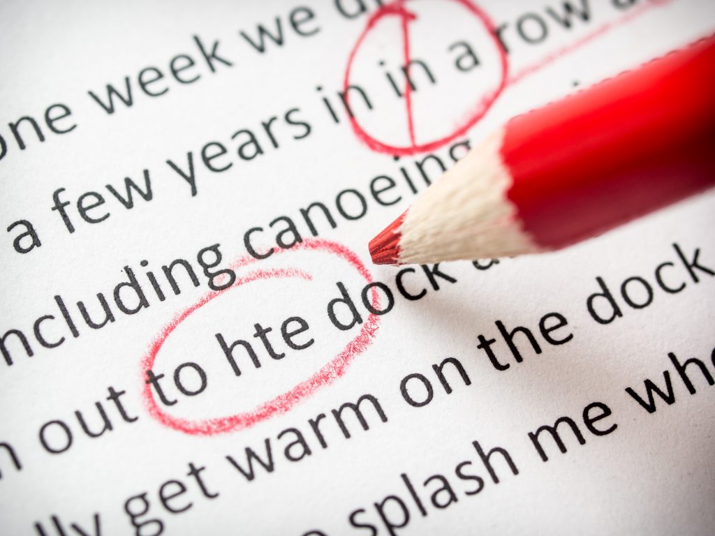 A typed document showing red proofreading and copy-editing marks with a red pencil at the ready to catch more errors.